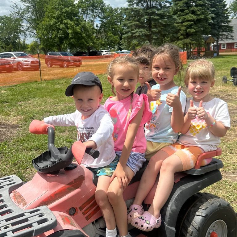 Kids smiling on a toy ATV outdoors